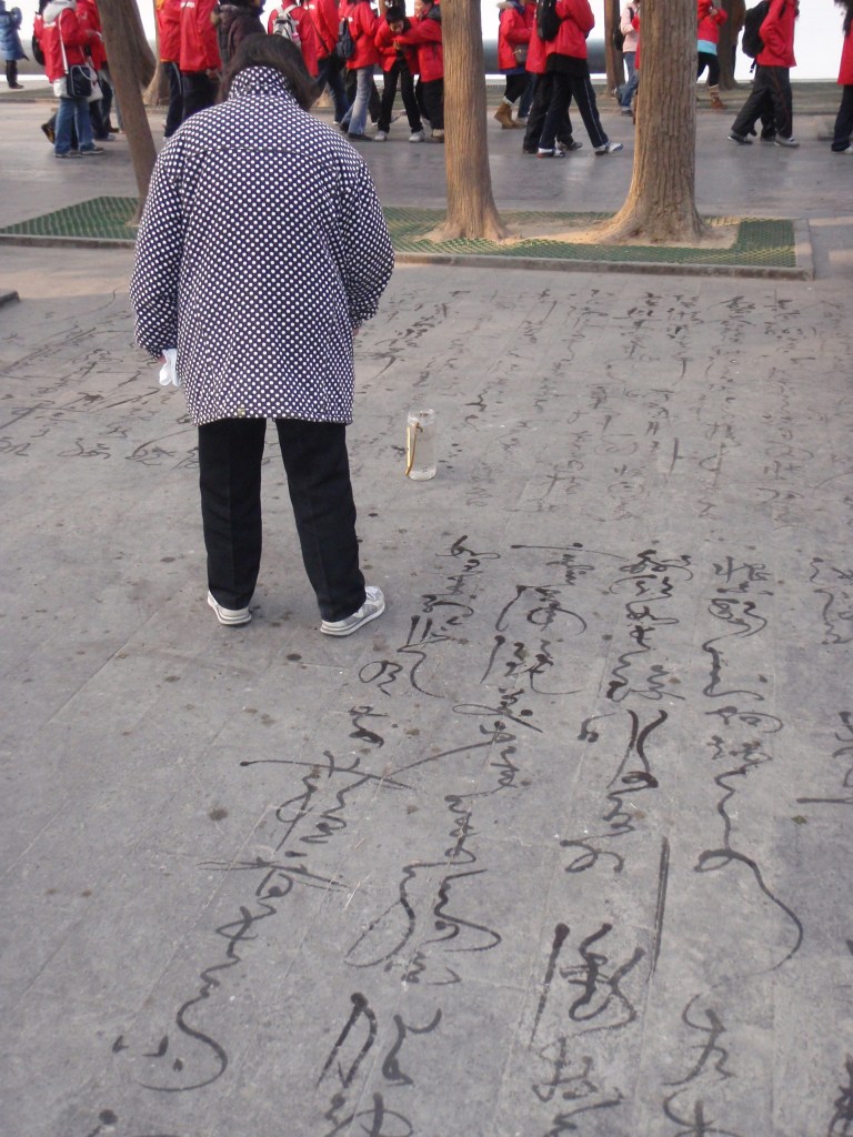 Elderly Chinese man practicing water calligraphy in a public square – Traditional Chinese street art