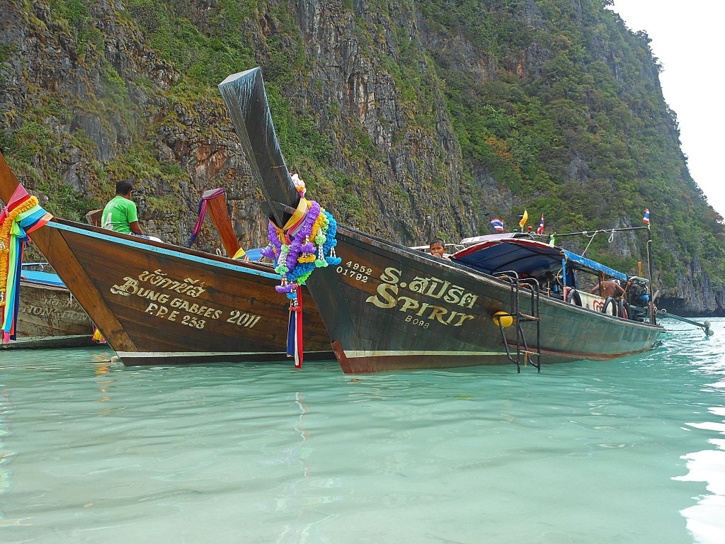 Traditional Thai long-tail boat floating in turquoise waters near limestone cliffs in Thailand