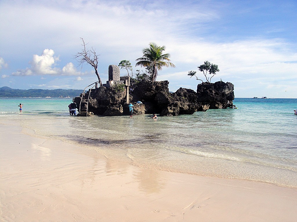 Willy's Rock shrine with Virgin Mary statue on white sand beach