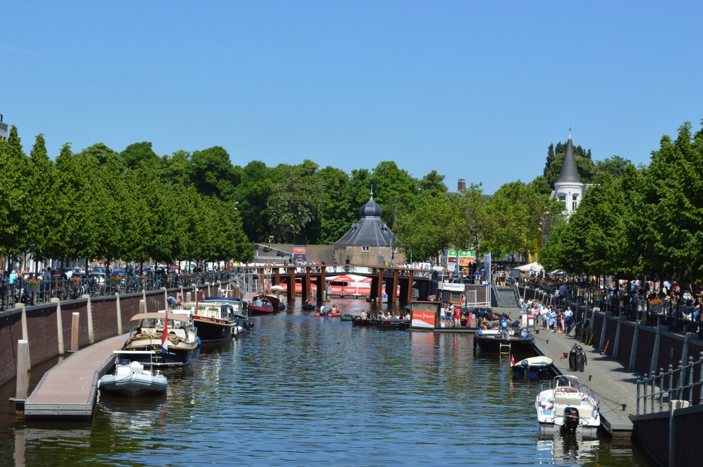 busy canal in breda netherlands with boats and weekend street market under blue sky