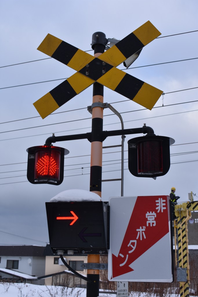 Japanese railway crossing with warning signs and red signal lights – Snow-covered winter scene