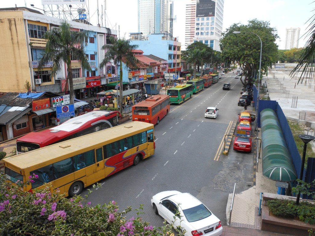 A busy street in Johor Bahru with colorful buses and high-rise buildings in the background.