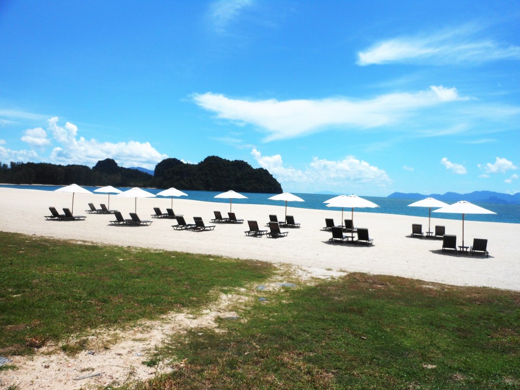 A tropical beach with lounge chairs and umbrellas under a clear blue sky.