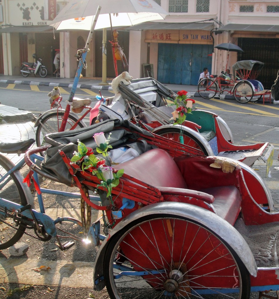 A colorful trishaw decorated with flowers parked on a street in George Town, Penang