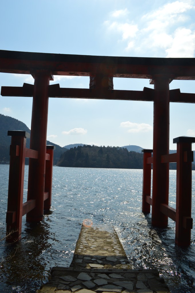 A red torii gate standing in the water of Lake Ashi, Hakone, with mountains in the background - Hakone stock photos