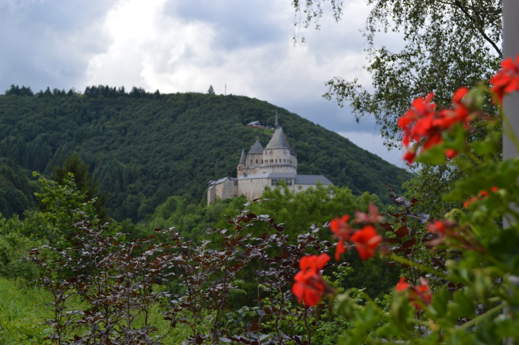 Vianden Castle in Luxembourg surrounded by forested hills with red flowers in the foreground - Luxembourg stock photos