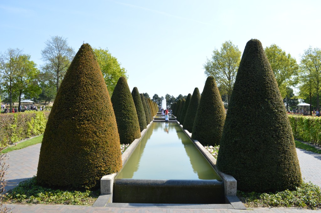 Symmetrical reflecting pool lined with tall manicured topiary trees at Keukenhof in the Netherlands. - Keukenhof stock photos
